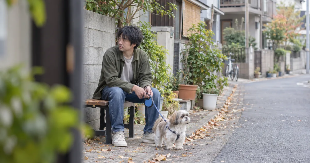 住宅街のベンチに座る30代の男性と、リードをつけたシーズー
